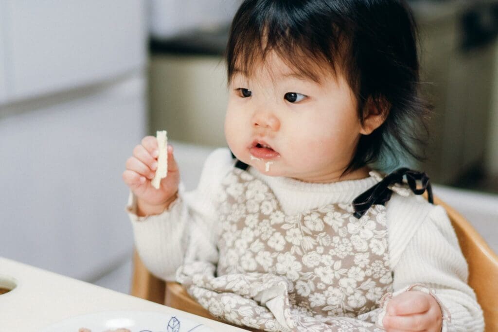 自宅の食卓で食べ物を持つ1歳前後の赤ちゃんの写真