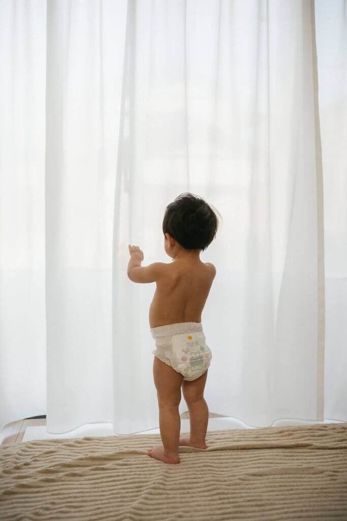 1歳前後の赤ちゃんが自宅の窓辺で立っている写真