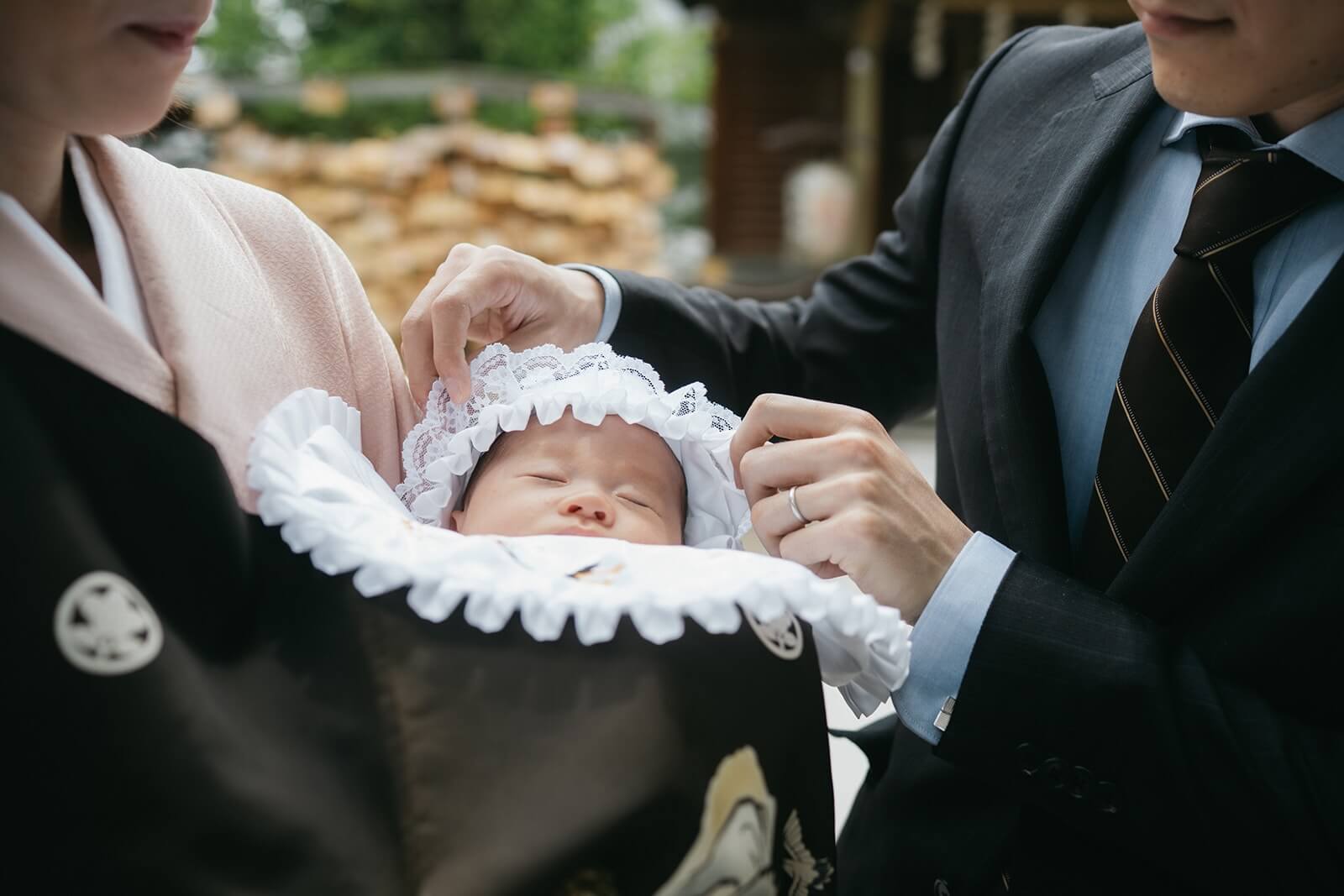 お宮参りで男の子の赤ちゃんの帽子に手を添える夫婦